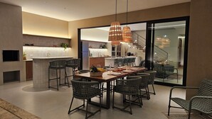 A modern dining area with a large table, wicker chairs, and pendant lighting. - Casa Aurora – Parque da Estalagem Condominium (Pirenópolis)