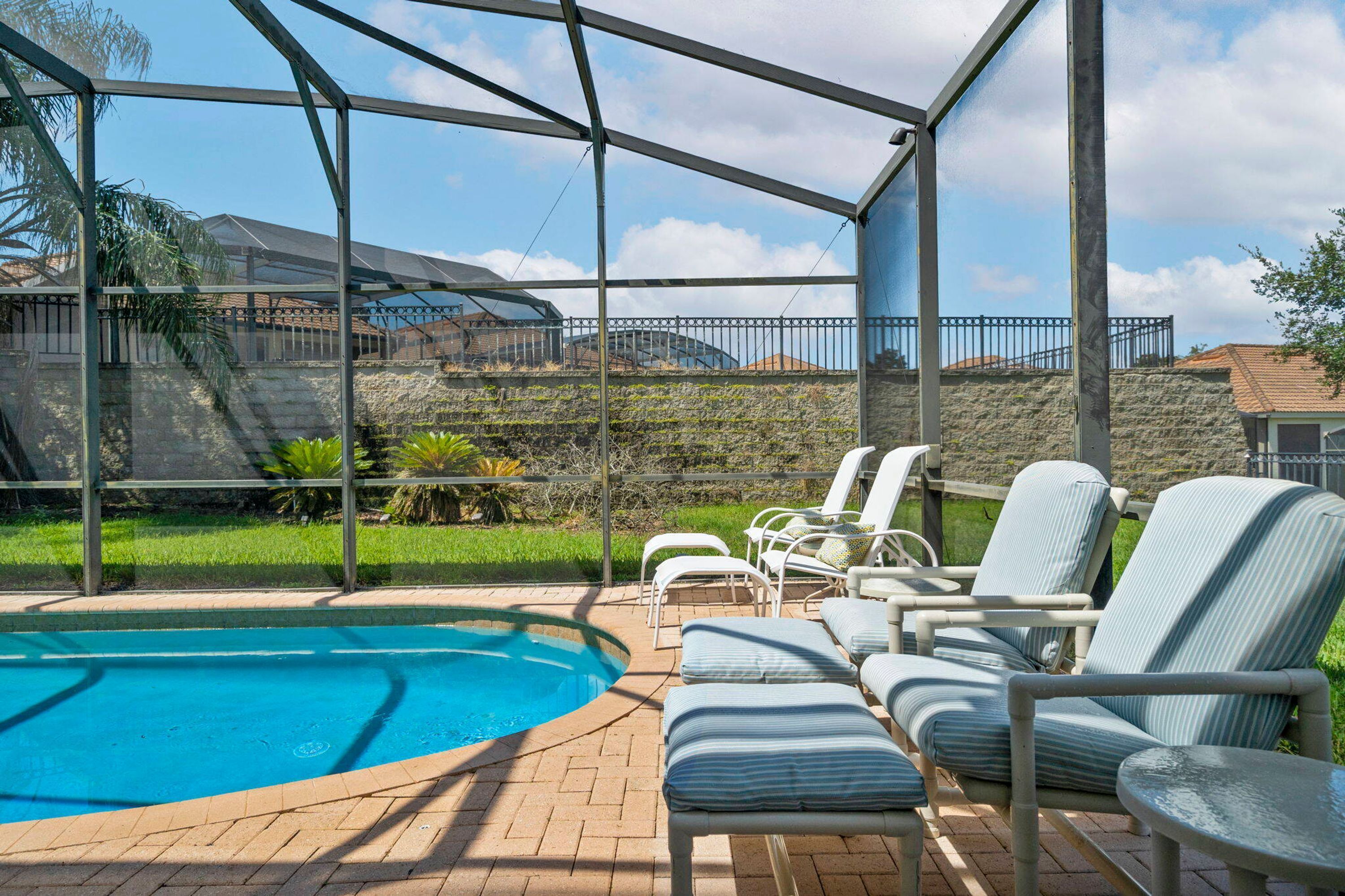 A pool area with a clear view of the sky, a stone wall, and a metal fence.