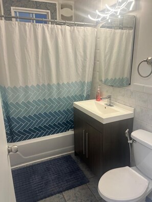Un baño con ducha, lavamanos, inodoro y espejo.