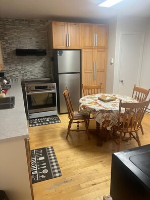 Una cocina con armarios de madera, un refrigerador de acero inoxidable, un horno y una mesa de comedor con sillas.