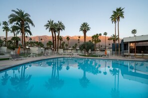 A swimming pool with lounge chairs and umbrellas, surrounded by palm trees and mountains in the background. - Whimsical mid-century mod at famed Ocotillo Lodge (Palm Springs)