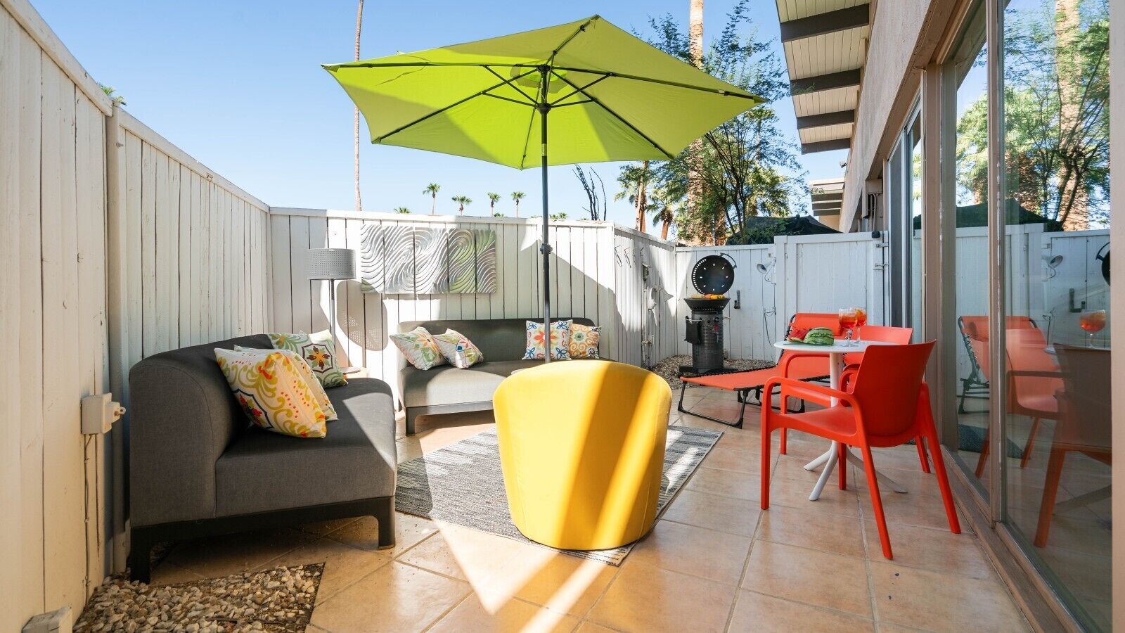 Eine Terrassengruppe im Freien mit einer Couch, einem gelben Hocker und roten Stühlen.
