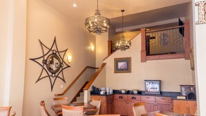 Zona de dinar amb cadires de vimetla, una decoració mural amb forma d'estrella i una escala que condueix a una zona de cuina amb armaris de fusta i una televisió.