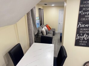 A dining area with a white marble table and black chairs, a grey sofa with cushions, and a wall with a motivational quote. - Delightful 3-bedroom apartment with AC in charming Johnston (Johnston)