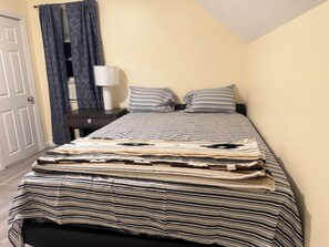A bedroom with a bed, pillows, a nightstand, a lamp, and a door.