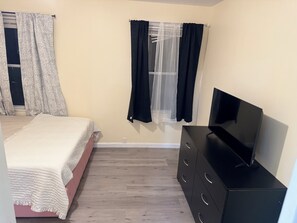 A bedroom with a bed, a dresser, a television, and a window with curtains. - Delightful 3-bedroom apartment with AC in charming Johnston (Johnston)