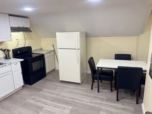 A compact kitchen with a stove, oven, and refrigerator, a dining table with chairs, and a light-colored floor. - Delightful 3-bedroom apartment with AC in charming Johnston (Johnston)
