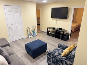 A living room with a flat-screen TV, a glass-top coffee table, a sofa, and a patterned armchair.