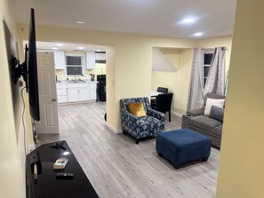 A living room with a sofa, ottoman, and a TV on a stand. - Delightful 3-bedroom apartment with AC in charming Johnston (Johnston)
