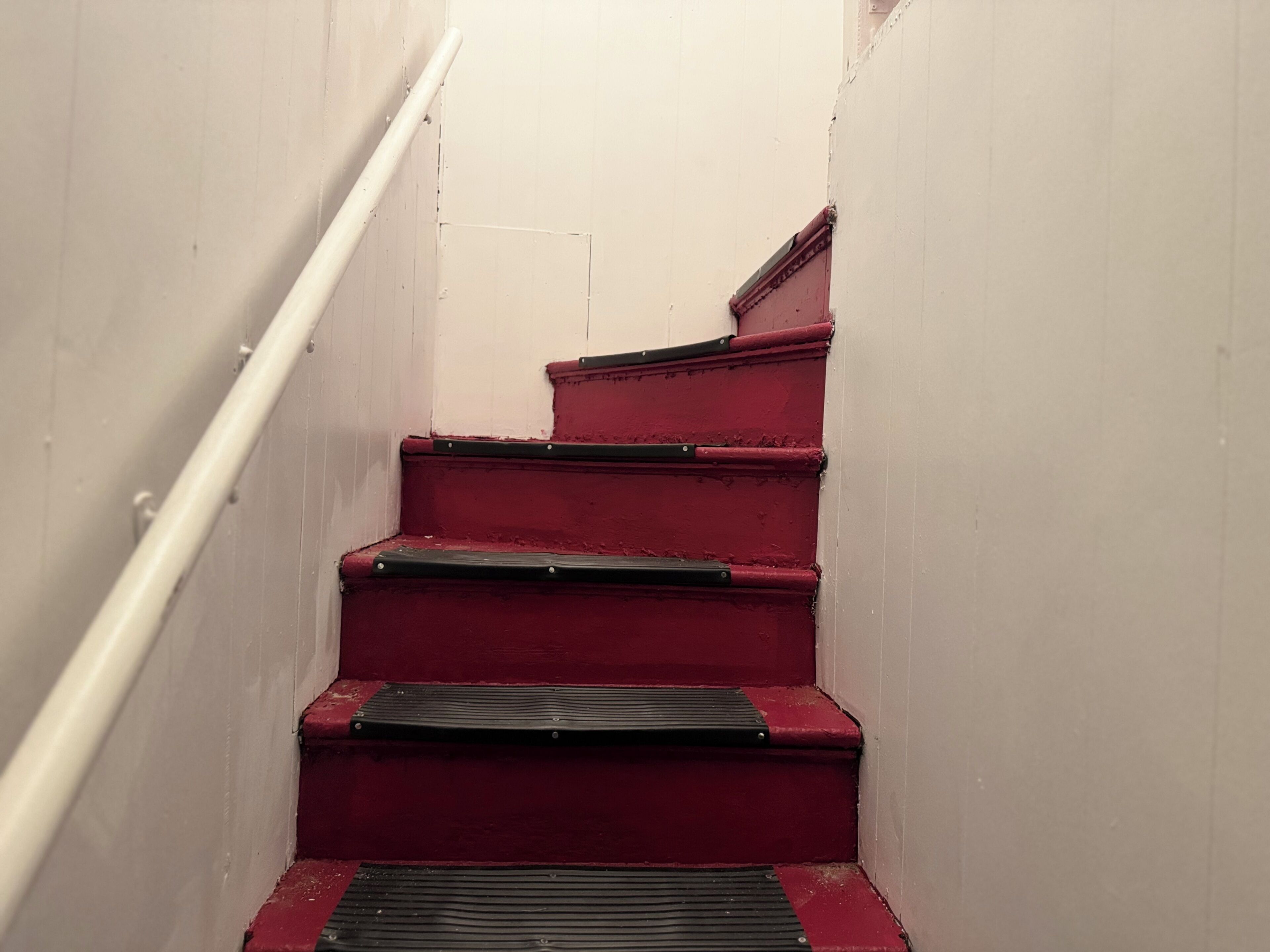 A set of red stairs with a handrail on the left, leading to a higher floor.