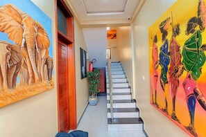 A hallway with a staircase, a potted plant, and two large wall murals. - COZY NEST Apt| Wi-Fi | Near town| Laundry Rm | Generator (Dar es Salaam)