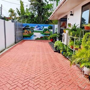 A paved pathway leading to a house with a mural of a landscape, surrounded by potted plants. - COZY NEST Apt| Wi-Fi | Near town| Laundry Rm | Generator (Dar es Salaam)