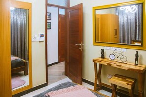 A bedroom with a bed, a bedside table with a bicycle model, a mirror, and a door leading to another room. - COZY NEST Apt| Wi-Fi | Near town| Laundry Rm | Generator (Dar es Salaam)