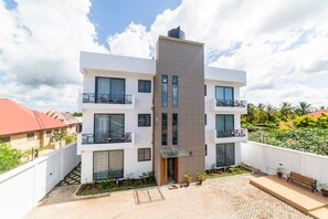 A modern multi-story building with balconies, a central entrance, and a paved courtyard. - 7 - Min Walk to Beach | Pool - KING Bed | Wi-Fi (Jambiani)