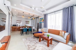 A modern living room with a sofa, coffee table, and dining area. - 7 - Min Walk to Beach | Pool - KING Bed | Wi-Fi (Jambiani)