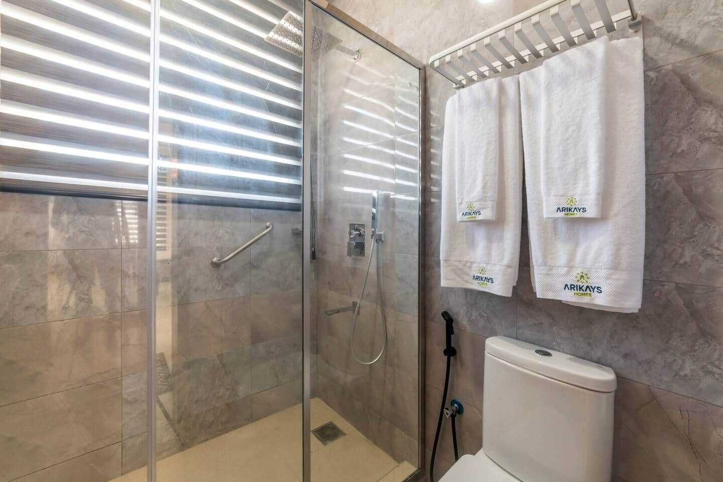 A bathroom with a glass-enclosed shower, a toilet, and two towels hanging on the wall.