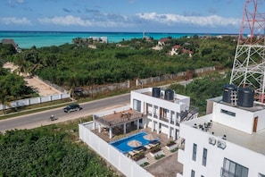 A modern building with a rooftop pool and water tanks, surrounded by greenery and a clear view of the ocean. - 7 - Min Walk to Beach | Pool - KING Bed | Wi-Fi (Jambiani)