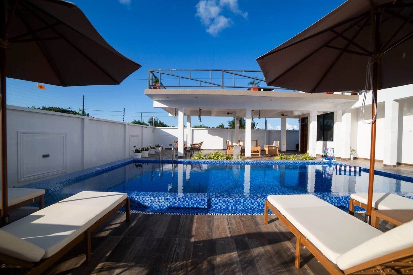 Una piscina con lettini e ombrelloni, circondata da un muro bianco e un pontile in legno.