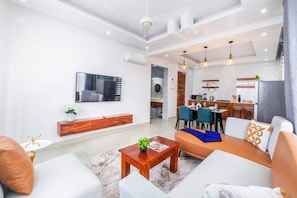 A modern living room with a sofa, coffee table, and a dining area with chairs and a table. - 7 - Min Walk to Beach | Pool - KING Bed | Wi-Fi (Jambiani)