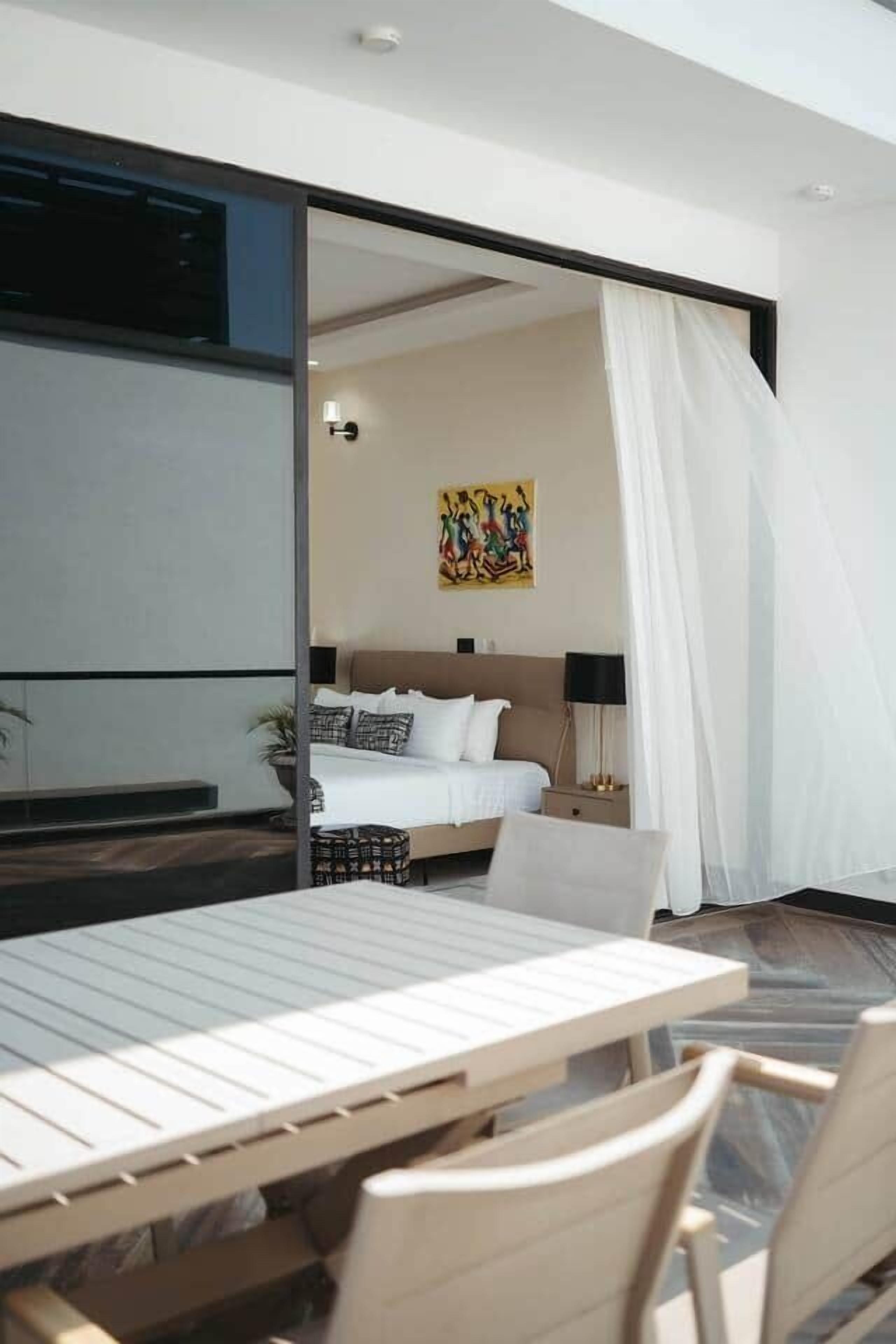 Una habitación de hotel moderna con cama, un cuadro, una mesita de noche y un rincón de comedor con mesa y sillas.