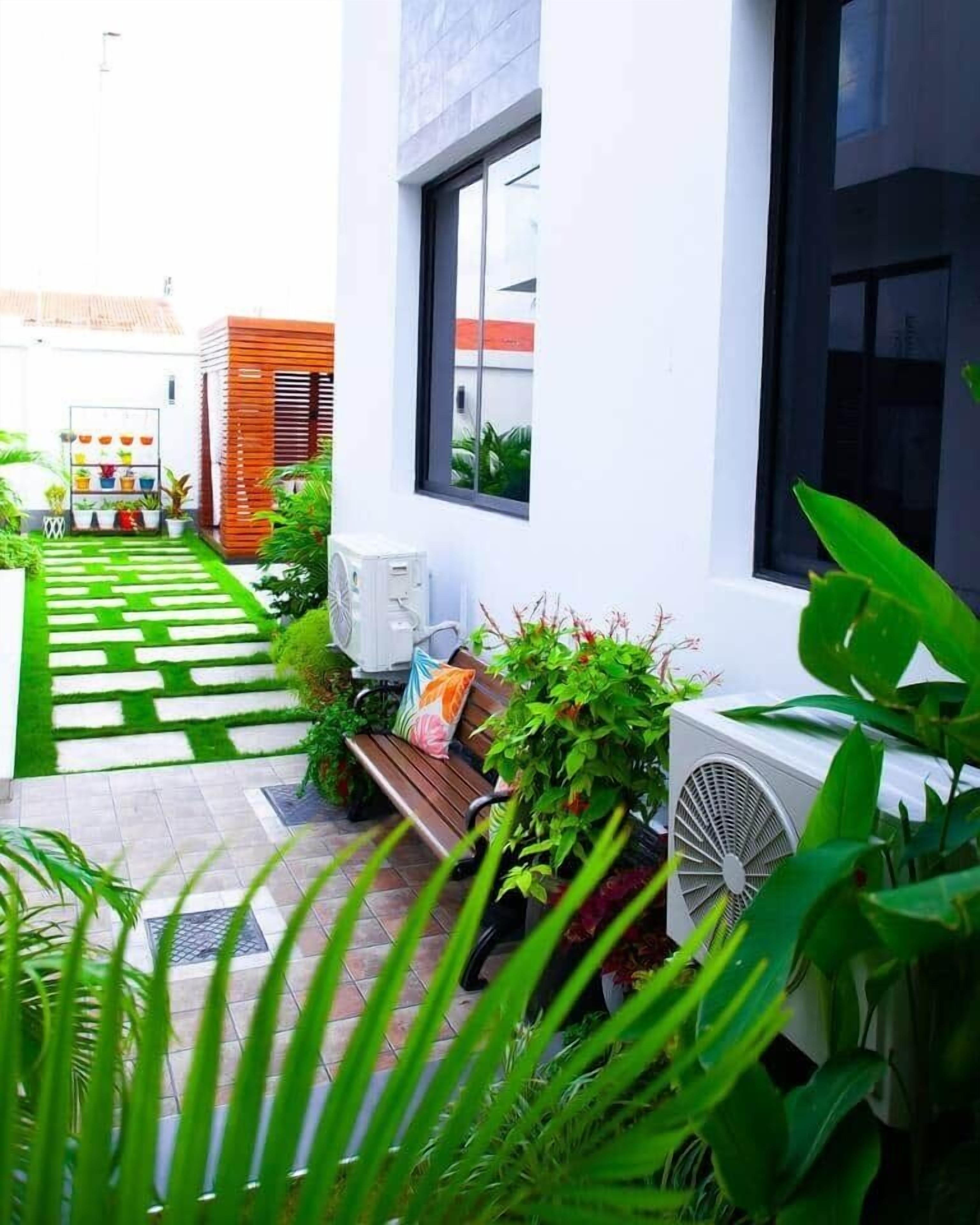 A modern outdoor area with a paved walkway, a bench, and a white wall with windows.