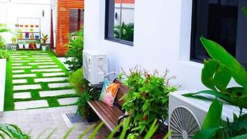A modern outdoor area with a paved walkway, a bench, and a white wall with windows.
