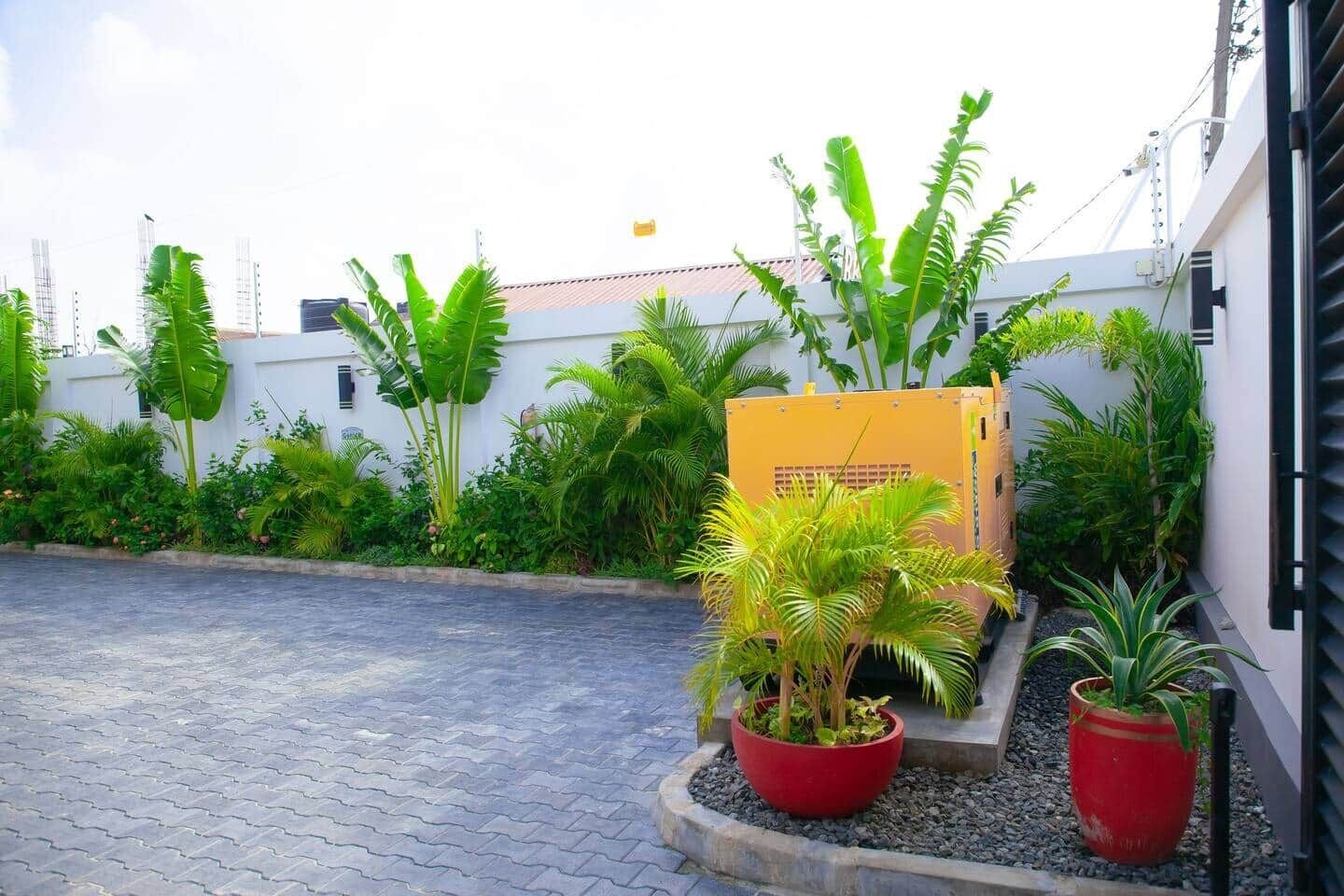 Une cour dallée, agrémentée de plantes en pot et surmontée d’une grande structure jaune.