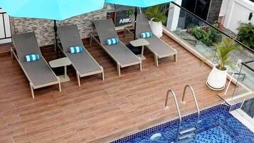 A rooftop pool area with lounge chairs and umbrellas, a tiled pool, and a modern building in the background.
