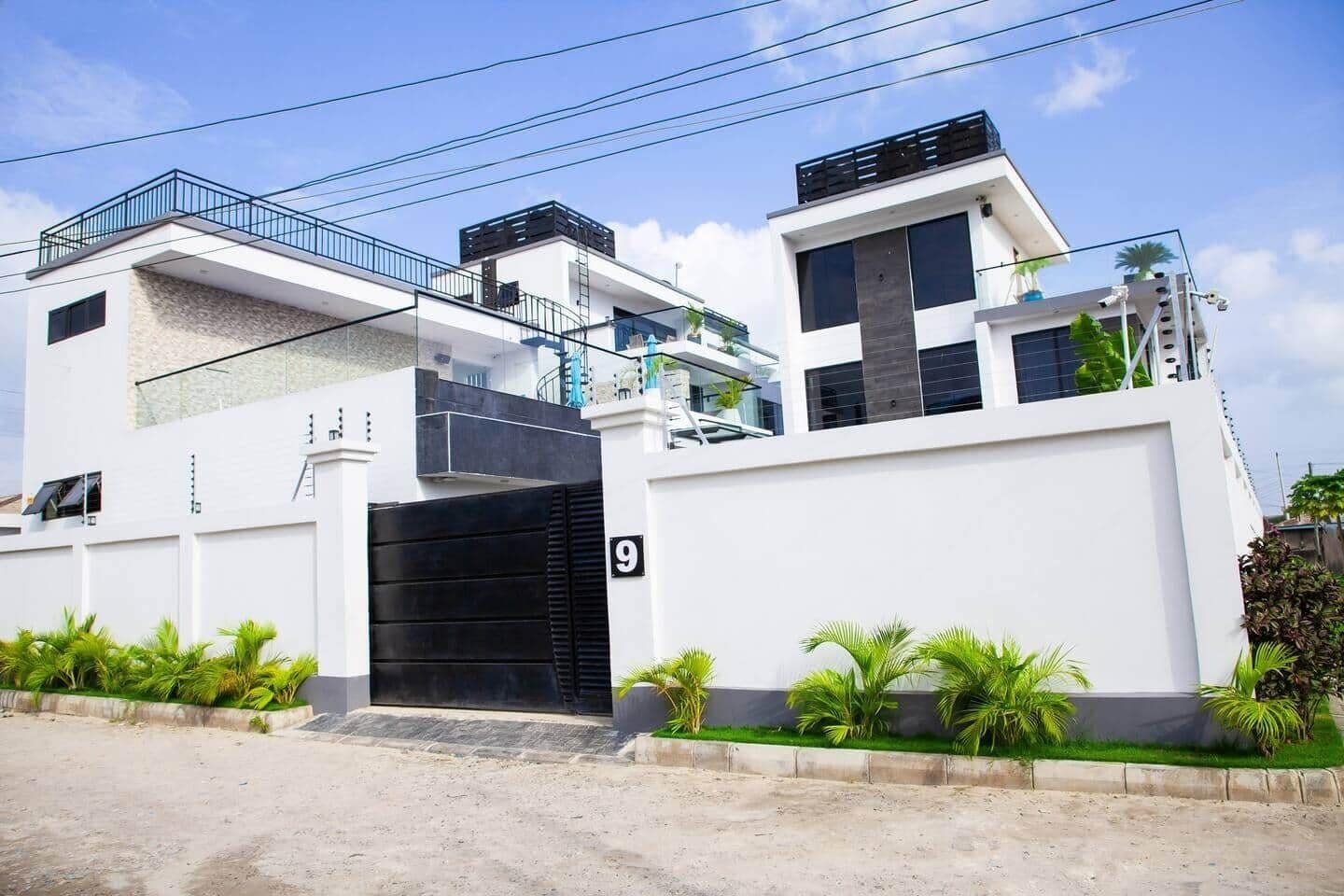 A modern two-story residential building with a black gate, number 9, and a balcony with a railing.