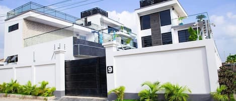 A modern two-story residential building with a black gate, number 9, and a balcony with a railing.