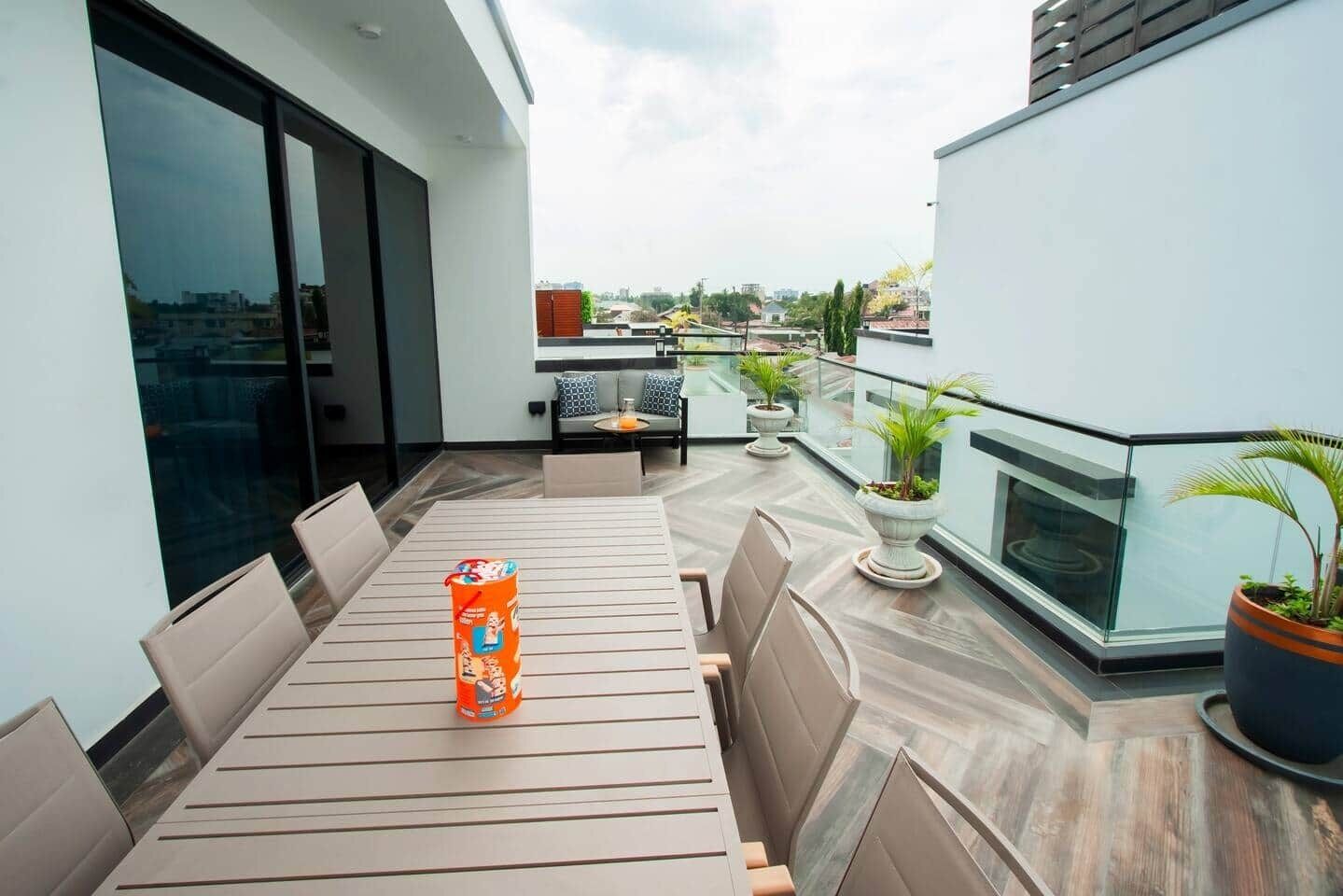 Un espace de repas extérieur moderne, avec une table et des chaises, un petit coin salon avec un canapé et une table, et des plantes en pot.
