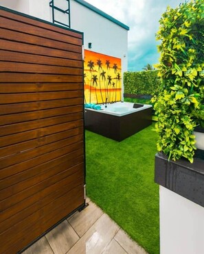 A modern outdoor area with a wooden fence, a hot tub, and a mural of palm trees. - Luxury Oasis 2BDR Apt. w/POOL - Jacuzzi - Gym - Near Mall (Dar es Salaam)