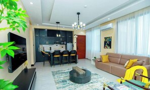 A modern living room with a sofa, a coffee table, and a dining area with chairs. - Luxury Oasis 2BDR Apt. w/POOL - Jacuzzi - Gym - Near Mall (Dar es Salaam)