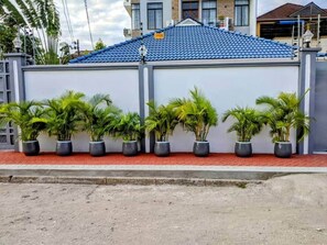A building with a blue tiled roof, a white wall, and a row of potted plants along the side. - The Sunrise Apt |Balcony view | Wi- FI | Near town (Dar es Salaam)