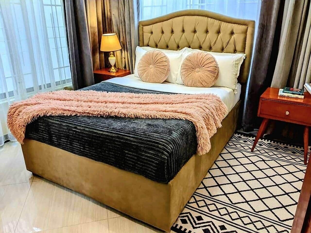 A bed with a tufted headboard, two pillows, a fluffy blanket, and a patterned rug.