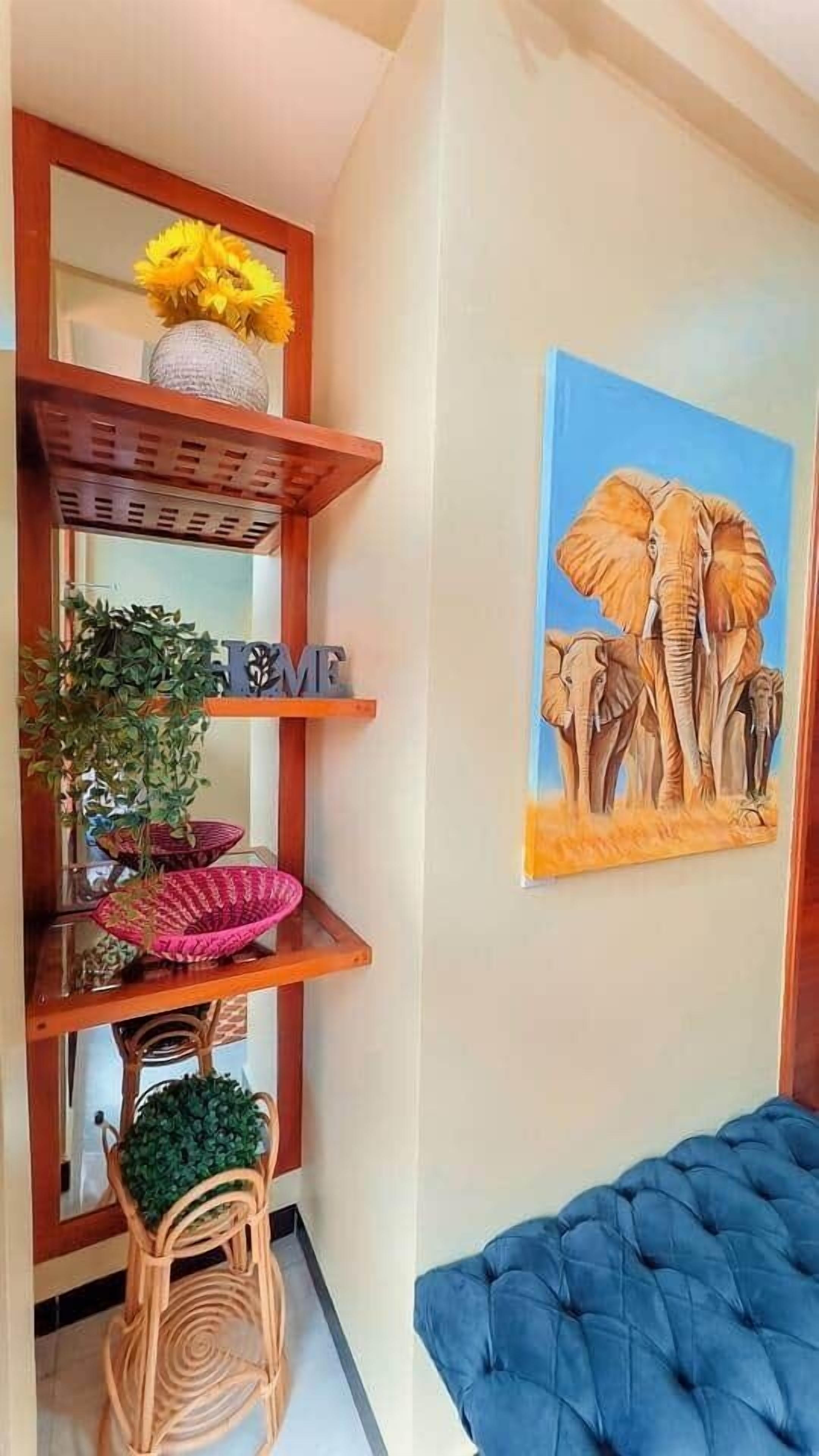 Une pièce avec un banc bleu rembourré, une étagère murale ornée d’objets décoratifs et un tableau représentant des éléphants.