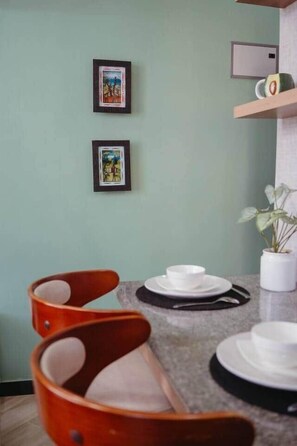 Un coin repas avec une table dressée pour deux personnes, deux tableaux encadrés au mur et une plante en pot posée sur le comptoir.
