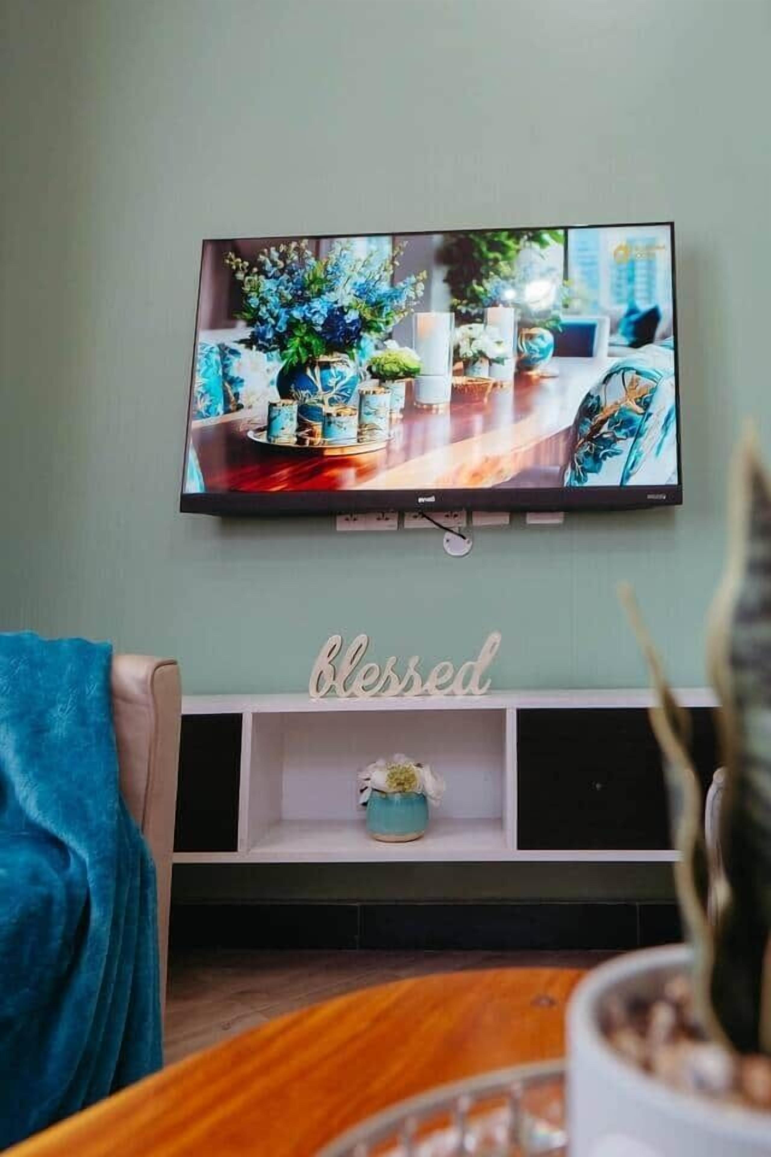 Un televisor de pantalla plana montado en una pared sobre un estante blanco con un letrero que dice 'Blessed'.