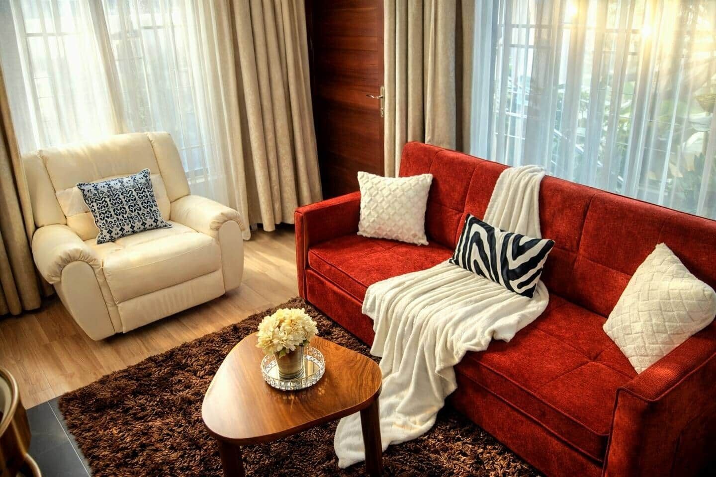 Un salon avec un canapé rouge, un fauteuil blanc et une table basse en bois sur laquelle est posé un vase de fleurs.