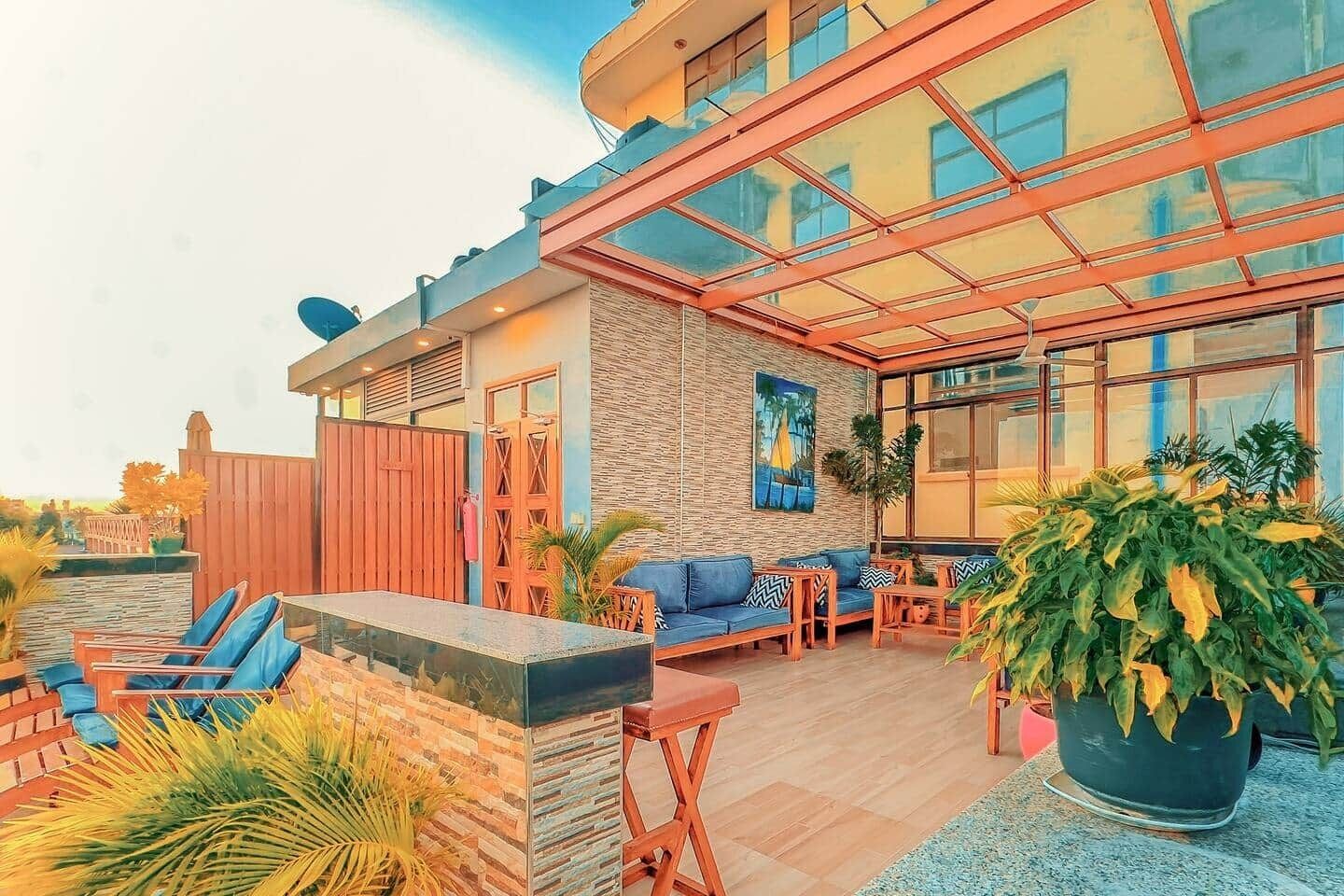 Un espacio de estar al aire libre cubierto, con techo de cristal, mobiliario de madera y plantas en macetas.