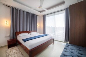 Ein Hotelzimmer mit einem großen Bett, einem Holz-Kopfende, einem Nachttisch, einem flauschigen Teppich und Blick auf die Stadt durch große Fenster.