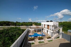A modern building with a pool, outdoor seating, and a view of the surrounding greenery. - Luxury Beachwalk Apt-Pool, King Bed-Rooftop Views (Jambiani Kikadini)