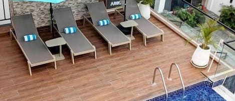 Un espace piscine sur le toit, avec des chaises longues et des parasols, une piscine carrelée et un bâtiment moderne en arrière-plan.