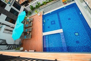 Ein moderner Hotelpoolbereich mit Holzterrasse, Liegestühlen und einem Pool mit blauem Mosaik.