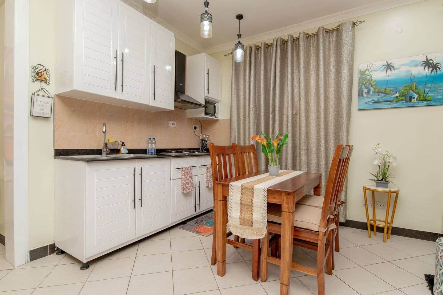 A compact kitchen with white cabinets, a dining table with chairs, and a small side table with a plant.