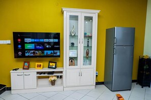Ein Wohnzimmer mit einem an der Wand montierten Flachbildfernseher, einer weißen Vitrine und einem grauen Kühlschrank.