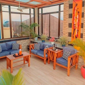 A sunlit room with a blue sofa set, wooden chairs, and a coffee table. - The Elegant | Spacious Apt | Near shopping (Dar es Salaam)