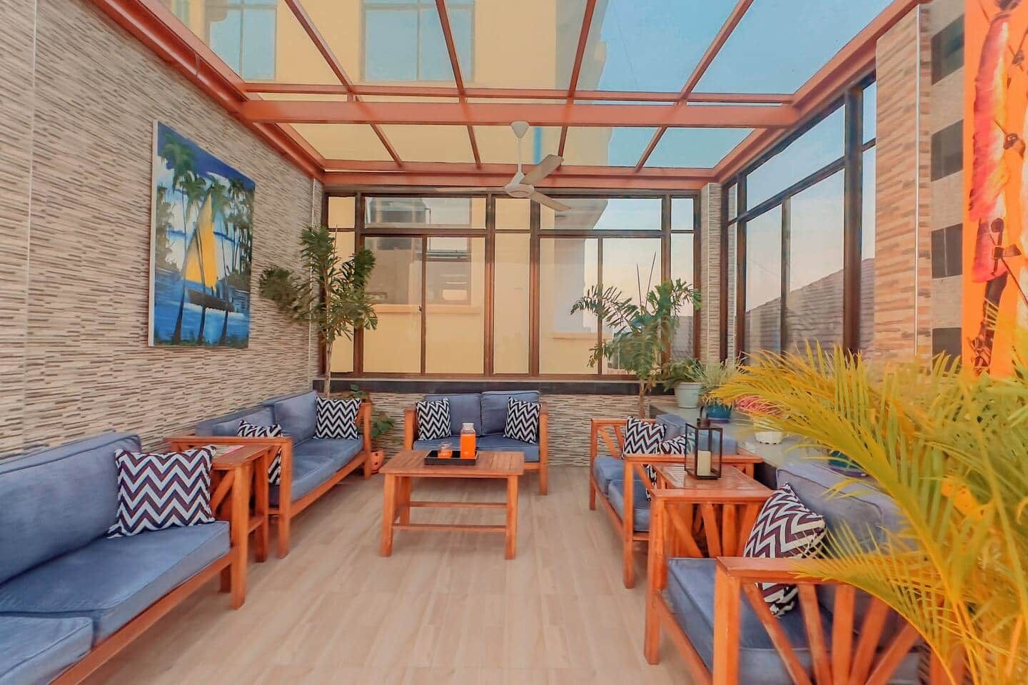 A sunlit indoor space with a glass ceiling, a sofa set, a coffee table, and potted plants.