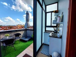 Ein kompakter Balkon mit einer kleinen Sitzecke, einem Gasherd und Blick auf die Stadtlandschaft.