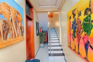 Um corredor com escada, um vaso de planta e duas grandes pinturas nas paredes.